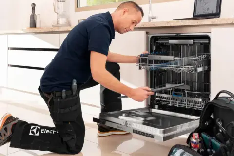 Serwisant w ubraniu z logo Electrolux naprawia zmywarkę. Electrolux to znana firma produkująca sprzęt AGD.