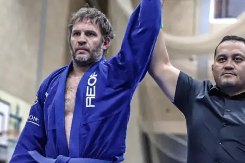 Tom Hardy i blå gi, med armen lyft som segrare i BJJ.