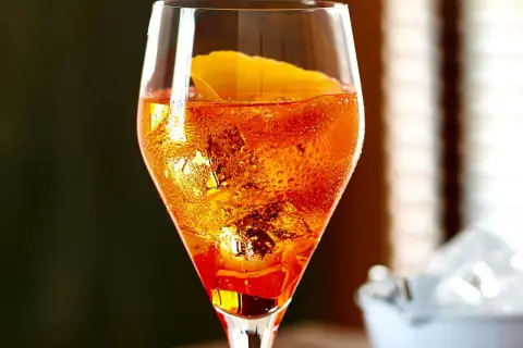 Ein Aperol Sour im Glas mit Eiswürfeln und Orangenzeste, Bläschen steigen auf.