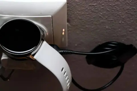 Biały smart bracelet podłączony do ładowarki w gniazdku. Dowiedz się, jak ładować swój smart bracelet.