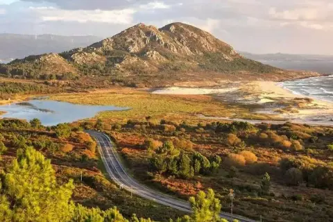 Carretera serpenteante hacia el monte Louro, con un lago, dunas y el mar al fondo.