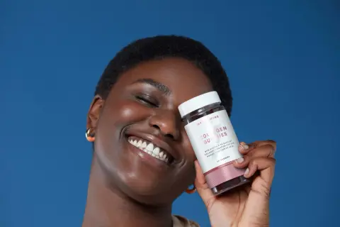 Mujer sonriente sostiene un frasco de gomitas de colágeno para la piel, con fondo azul.