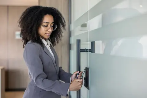 Donna con afro e occhiali usa lo smartphone per la rilevazione presenze, aprendo una porta in vetro.