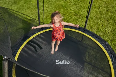 Ein fröhliches Mädchen springt auf einem Trampolin. Die Frage "Trampolin ab welchem Alter?" stellt sich hier nicht, denn Spaß kennt kein Alter!