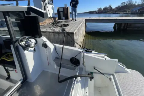 En vit båt vid en brygga. Vattnet är klart och man kan se alger i diesel-färgat vatten.