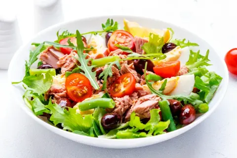 En fräsch sallad nicoise med tonfisk, ägg, tomater, gröna bönor och oliver på en bädd av grönsallad.