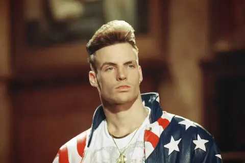 Homme blond avec une coiffure audacieuse, portant une veste aux couleurs du drapeau américain.