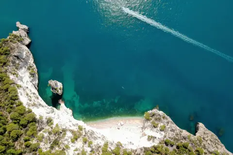Vista aerea della cala della pipa, con scogliere bianche, vegetazione verde e mare turchese. Una barca lascia una scia sull'acqua.