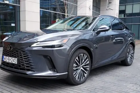 Elegancki, ciemnoszary Lexus RX 450h z nowoczesnym grillem i felgami stoi przed budynkiem biurowym.