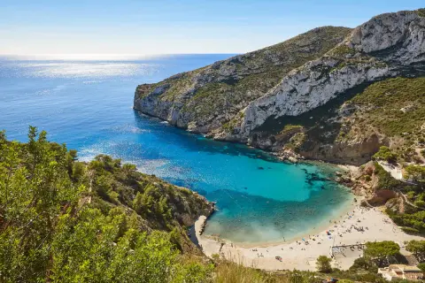 Bahía de aguas turquesas y arena dorada, rodeada de acantilados verdes. Un paraíso de playas bonitas con gente disfrutando del sol.