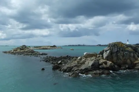 Îles rocheuses et mer turquoise près de Douarnenez, avec la Pointe du Raz en arrière-plan sous un ciel menaçant.