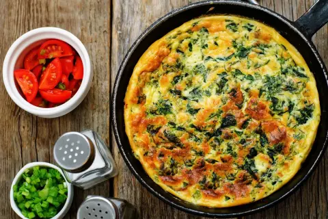 Frittata ze szpinakiem i serem, idealna jako pomysł, czym zastąpić węglowodany. Obok pomidorki i szczypiorek.