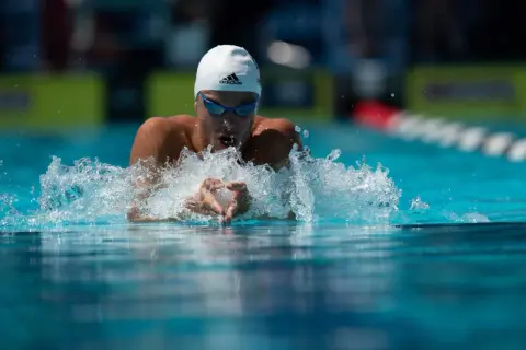 Swimmer executing perfect breaststroke technique, arms pulling water, creating a splash.