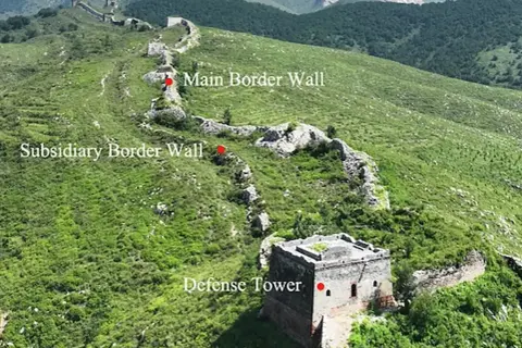 La muralla china se extiende por colinas verdes, con una torre de defensa y muros principales y subsidiarios.