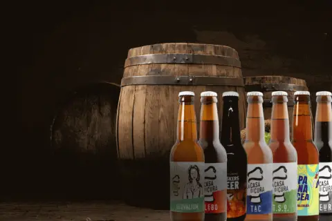 Bottiglie di birra artigianale davanti a botti di legno, un'atmosfera da keller pub.