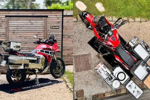 Una moto trail roja lista para la aventura, con maletas y equipo de camping.