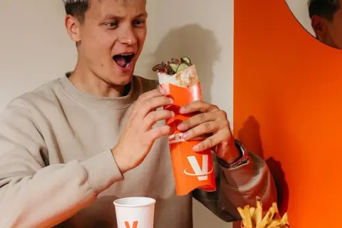 Młody mężczyzna z zachwytem trzyma w rękach viral kebab. Jego mina sugeruje, że opinie o tym daniu są w pełni uzasadnione.