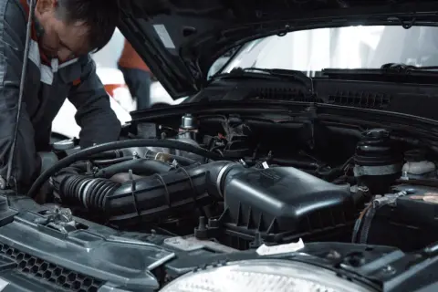 Mechanik w kombinezonie pracuje przy silniku samochodu, być może wykonując procedurę jak odpowietrzyć sprzęgło.