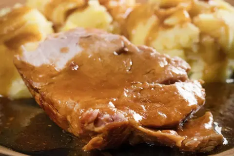 Mięciutka karkówka w sosie, podana z purée ziemniaczanym. Danie wygląda apetycznie i sycąco.