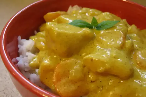 Miseczka czerwona z ryżem i kremowym, żółtym curry z kawałkami kurczaka i marchewki, ozdobiona listkiem mięty.