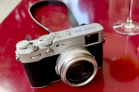 Appareil photo argenté Fujifilm X100VI sur fond rouge vif, prêt pour un test.