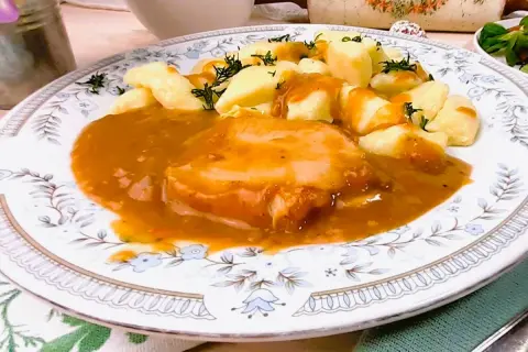 Pyszny schab w sosie, podany z kluskami śląskimi i posypany koperkiem. Danie prezentuje się apetycznie na ozdobnym talerzu.