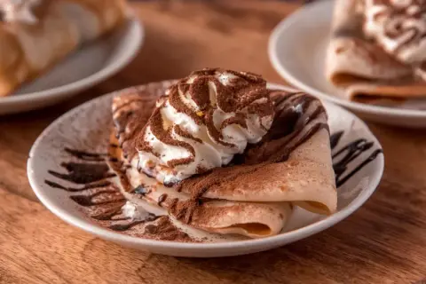 Deliziose crepes senza uova, guarnite con panna montata, cacao e sciroppo al cioccolato, un piacere per gli occhi e il palato.