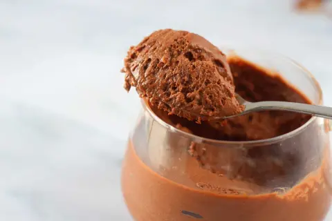 Un cucchiaio raccoglie una porzione generosa di soffice mousse al cioccolato da un bicchiere trasparente.