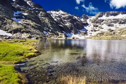 Espectacular vista de la ruta laguna grande de Gredos, con montañas nevadas, césped verde y aguas cristalinas.