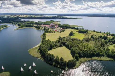 Żaglówki na jeziorze koło pałacu w Krainie Wielkich Jezior Mazurskich. Nietypowe atrakcje Podlasia to także piękne krajobrazy i sporty wodne.