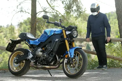 Motocicleta azul de estilo neo retro con detalles dorados, aparcada junto a un hombre con casco.