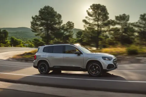 Nowy Mercedes GLB sunie po krętej drodze wśród drzew.