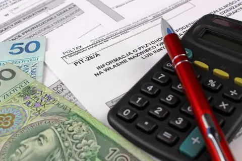 Polskie banknoty, formularz PIT-28/A, kalkulator i czerwony długopis.