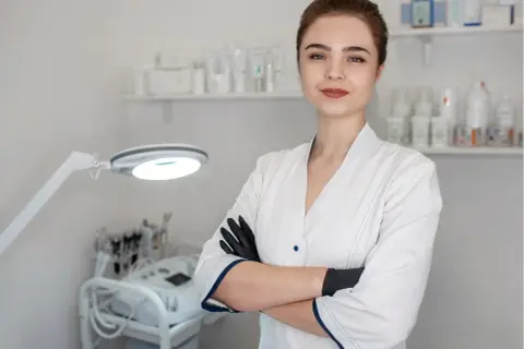Młoda kosmetolog w gabinecie, gotowa do zabiegu. W tle sprzęt i kosmetyki.