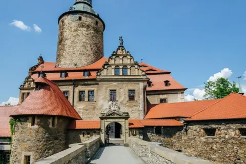 Zamek Czocha, malownicza trasa turystyczna. Kamienne mury, czerwone dachy i wieża zamkowa pod błękitnym niebem.