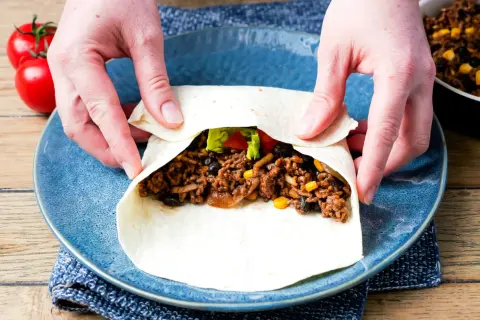 Hände falten wraps mit Hackfleisch, Bohnen und Mais. Ein leckerer Snack wird zubereitet.