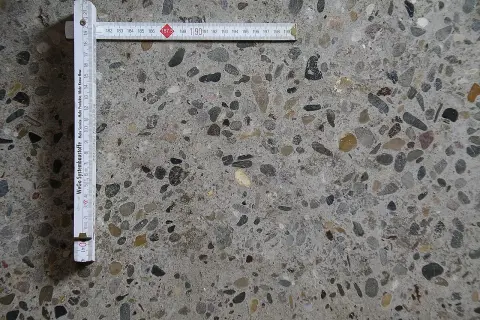 Superficie di calcestruzzo a vista con aggregati di varie dimensioni. Un righello pieghevole misura la **classe di esposizione calcestruzzo**.
