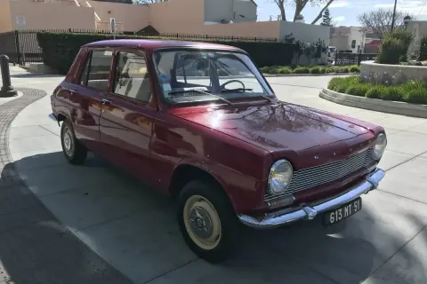 En röd Simca 1100 står parkerad på en solig uppfart.