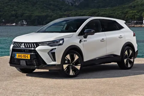 Nowy model Mitsubishi, biały SUV z czarnym dachem, stoi nad wodą. Nowoczesne linie i felgi podkreślają jego dynamiczny charakter.