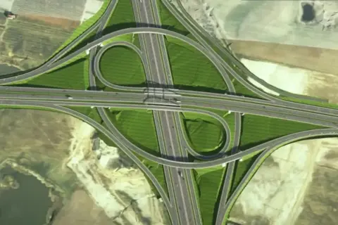 Widok z lotu ptaka na skomplikowany węzeł drogowy, część obwodnicy metropolitalnej Trójmiasta, z zielonymi terenami i wijącymi się estakadami.