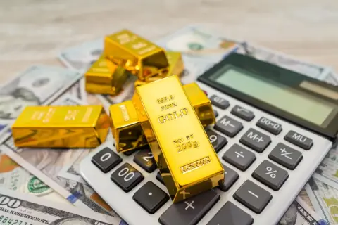 Sztabki złota na banknotach dolarowych i kalkulatorze symbolizują mądry gold investment.