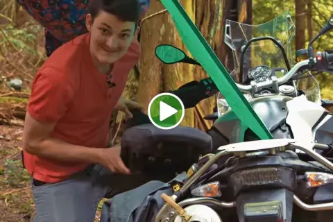 Mężczyzna przygotowuje motocykl do moto campingu w lesie, pakując bagaż.