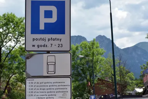 Znaki parkingowe w Zakopanem, informujące o płatnym postoju i cenniku. W tle góry i drzewa, idealne na trasę do skoczni.