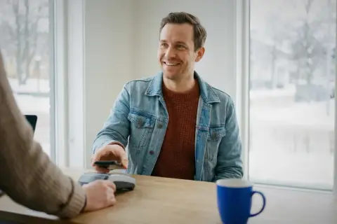 Uśmiechnięty mężczyzna płaci telefonem w Szwecji. Choć gotówka jest rzadkością, nadal można nią płacić.
