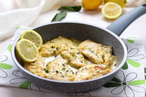 Scaloppine di pollo al limone in padella, guarnite con spicchi di limone fresco e prezzemolo tritato.