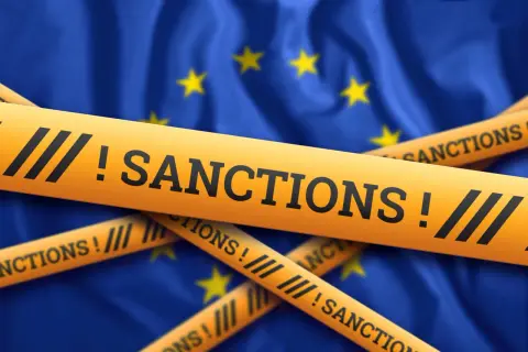 Żółte taśmy z napisem "SANCTIONS!" przecinają flagę Unii Europejskiej, symbolizując nałożone sankcje.