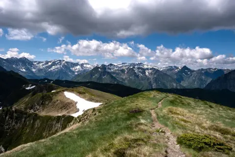 Sentier rocailleux menant vers le pic de Tarbesou, avec des montagnes enneigées en arrière-plan sous un ciel nuageux.