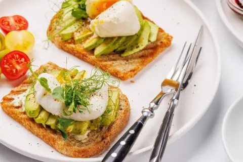 Zwei Scheiben Toast mit Avocado und pochiertem Ei, garniert mit Sprossen. Ein köstliches Egg Benedict Avocado Gericht.