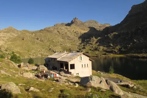 Refuge de montagne au bord d'un lac, idéal pour une randonnée vallée des merveilles 2 jours. Des randonneurs se reposent.