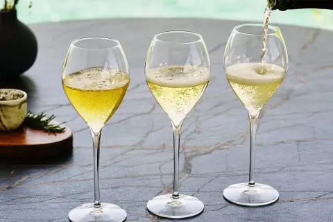 Trzy kieliszki wypełnione musującym winem. Jedno z nich jest nalewane z butelki. To jest właśnie cava!